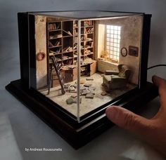 a hand is holding a miniature model of a living room