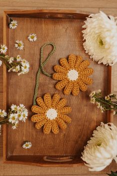 two crocheted flowers sitting on top of a wooden tray next to white flowers