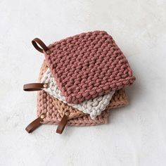 three crocheted dishcloths are stacked on top of each other with brown leather handles