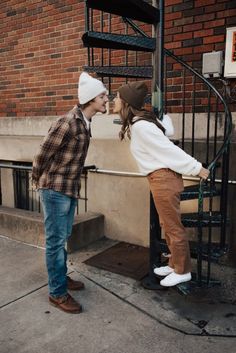 a young man and woman kissing on the steps in front of a brick apartment building