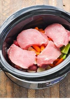 raw meat and vegetables in an electric pressure cooker on a wooden table with tongs