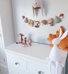 a white dresser topped with lots of stuffed animals next to a wall mounted deer head