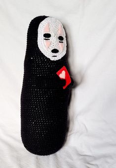 a knitted black bag with a white mask on it and a red heart in the pocket