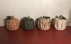 four small pumpkins sitting on top of a red table next to a white wall