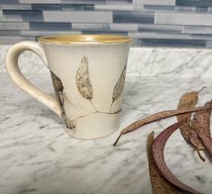 a white coffee cup sitting on top of a marble counter next to a leafy plant