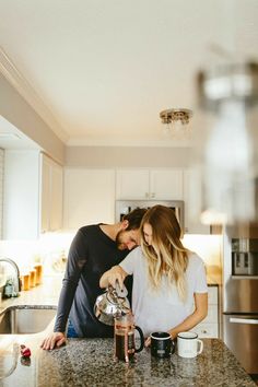 a man and woman standing in a kitchen next to each other pouring something into a cup