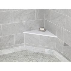 the corner of a bathroom with gray marble tile and white shelf for soap dispenser