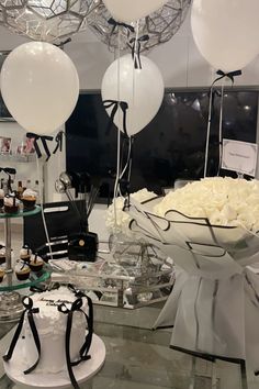 a bunch of white balloons are hanging from the ceiling above a table with cakes and cupcakes