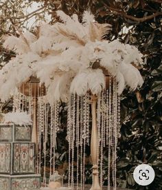 a table topped with a vase filled with white flowers and feathers hanging from it's sides