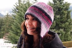 a woman wearing a multicolored crocheted hat smiling at the camera with trees in the background