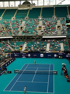 two people playing tennis on a blue court in front of an audience at a sporting event