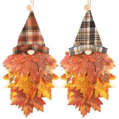 two fall leaf decorations hanging from hooks on a white wall, one with a plaid hat and the other decorated with autumn leaves