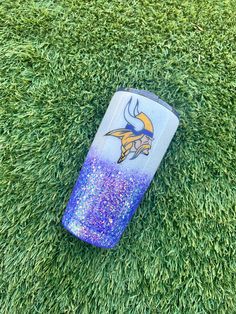 a blue and purple tumbler laying on top of green grass with a minnesota logo painted on it