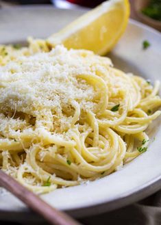 a plate of pasta with parmesan cheese and lemon wedges on the side