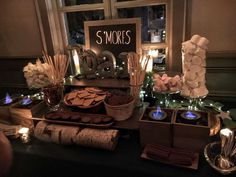 a table topped with lots of desserts and candles next to a sign that says s'mores