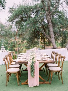 a table set up for a wedding with white linens and greenery