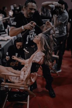 a woman sitting in a chair while another person cuts her hair