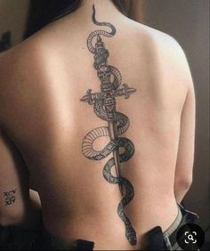 a woman's back with a snake and dagger tattoo on her left side ribcage