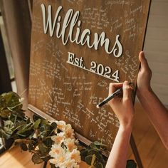 a person writing on a wooden sign with flowers