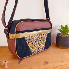 a brown and blue purse sitting on top of a wooden table next to a potted plant