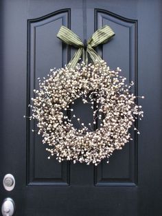 a black door with a green bow and white flowers on the front, is decorated with baby's breath