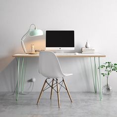 a desk with a computer on it next to a white chair and potted plant