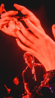 a man holding a guitar in front of his face while performing on stage with two hands behind him