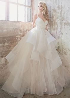 a woman standing in front of a window wearing a wedding dress with ruffled layers