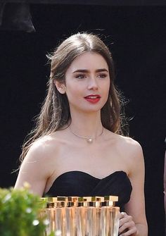 a woman in a strapless black dress holding a stack of gold cups and looking at the camera