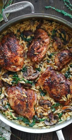 chicken and rice dish in a pan on a wooden table with green sprigs