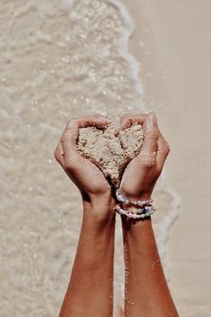 two hands holding sand in front of the ocean