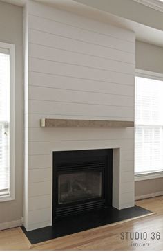 an empty living room with a fireplace and two windows in the corner, all painted white