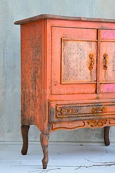 an old wooden cabinet with ornate carvings on the doors and drawers is painted orange in color