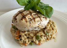 a white plate topped with chicken and rice covered in sauce, garnished with green leaves