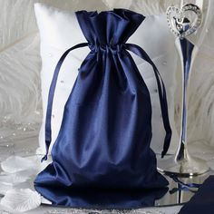 a blue satin bag sitting on top of a white pillow next to a silver vase