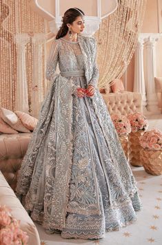 a woman in a blue and silver wedding gown standing next to a couch with flowers on it