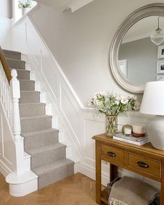 a vase with flowers sitting on top of a wooden table next to a stair case