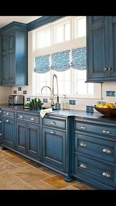 a kitchen with blue cabinets and tile flooring, along with a bowl of fruit on the counter