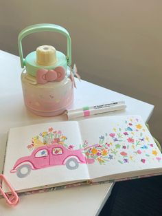 an open book sitting on top of a table next to a cup and marker pen