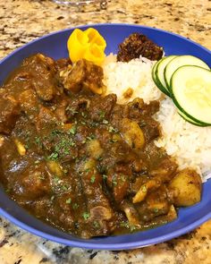 a blue plate topped with rice and meat next to cucumbers on a counter