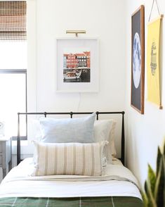 a bed with white sheets and pillows in a bedroom next to two pictures on the wall