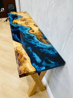 a wooden table with blue and yellow paint on it's surface, sitting in front of a white wall