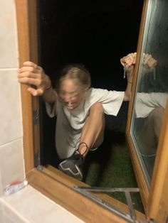 a man in white shirt and black shoes looking through window with hand on door handle