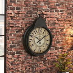 a clock mounted to the side of a brick wall next to a potted plant