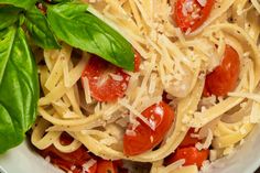 a white bowl filled with pasta, tomatoes and basil on top of a wooden table