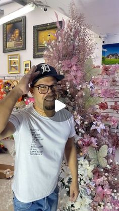 a man wearing glasses and a baseball cap standing in front of a display of flowers