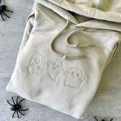 two white hooded sweatshirts with embroidered ghost faces on them and spider webs in the background