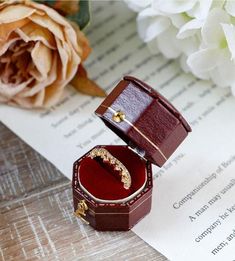 an open ring box sitting on top of a piece of paper next to a flower