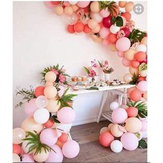 a table topped with lots of balloons next to a wall filled with flowers and greenery