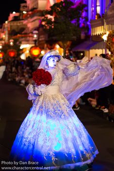 a woman in a white dress with red flowers on her head is walking down the street